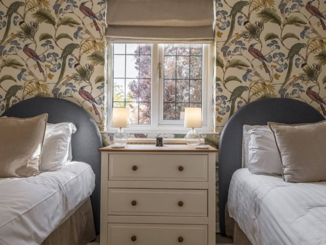 Twin bedroom with bird-print wallpaper and two upholstered headboards, St Hilary's House